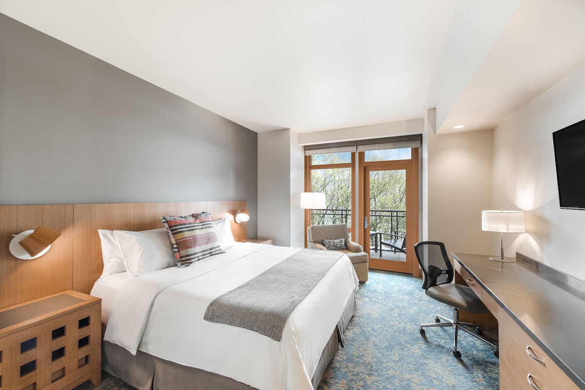 A hotel room with a bed, bedside tables, a desk, a chair, and a balcony with a view.