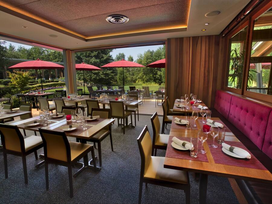 Ein Restaurant mit mehreren Tischen und Stühlen, roten Sonnenschirmen und Blick auf den Garten.