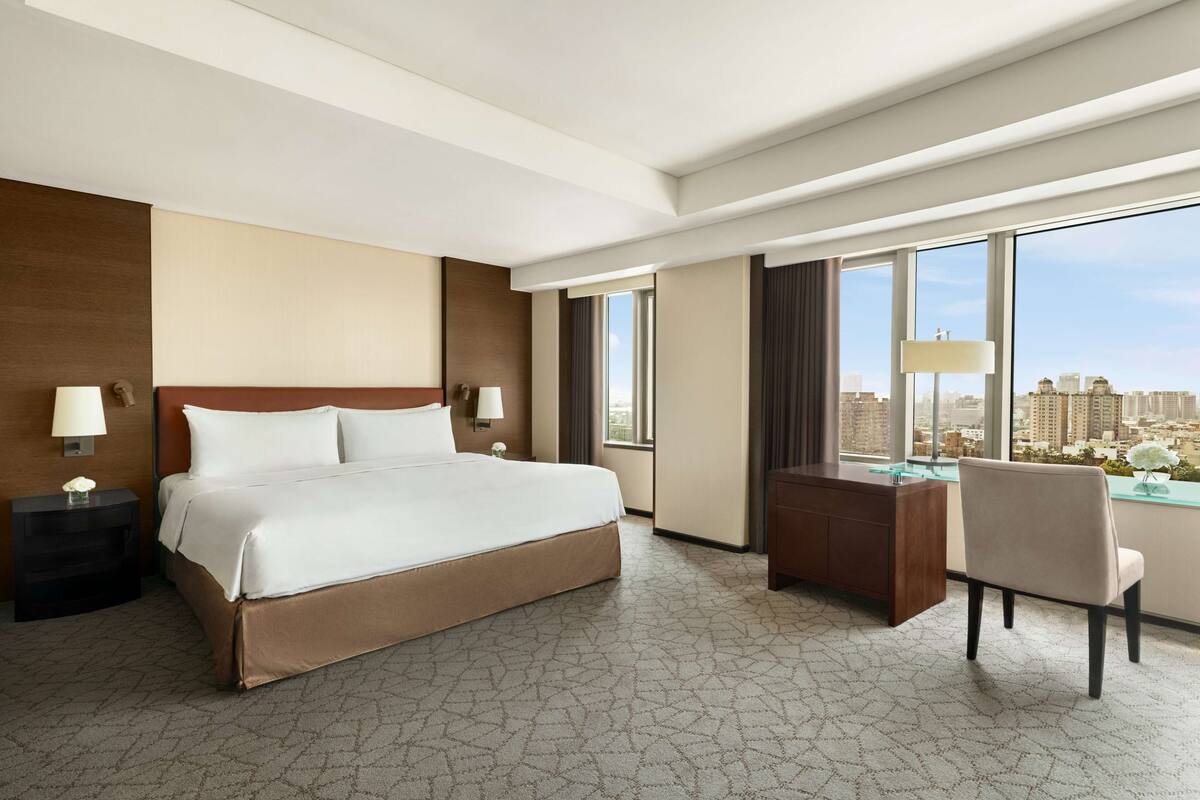 Een hotelkamer met een groot bed, een bureau en uitzicht op de stad.