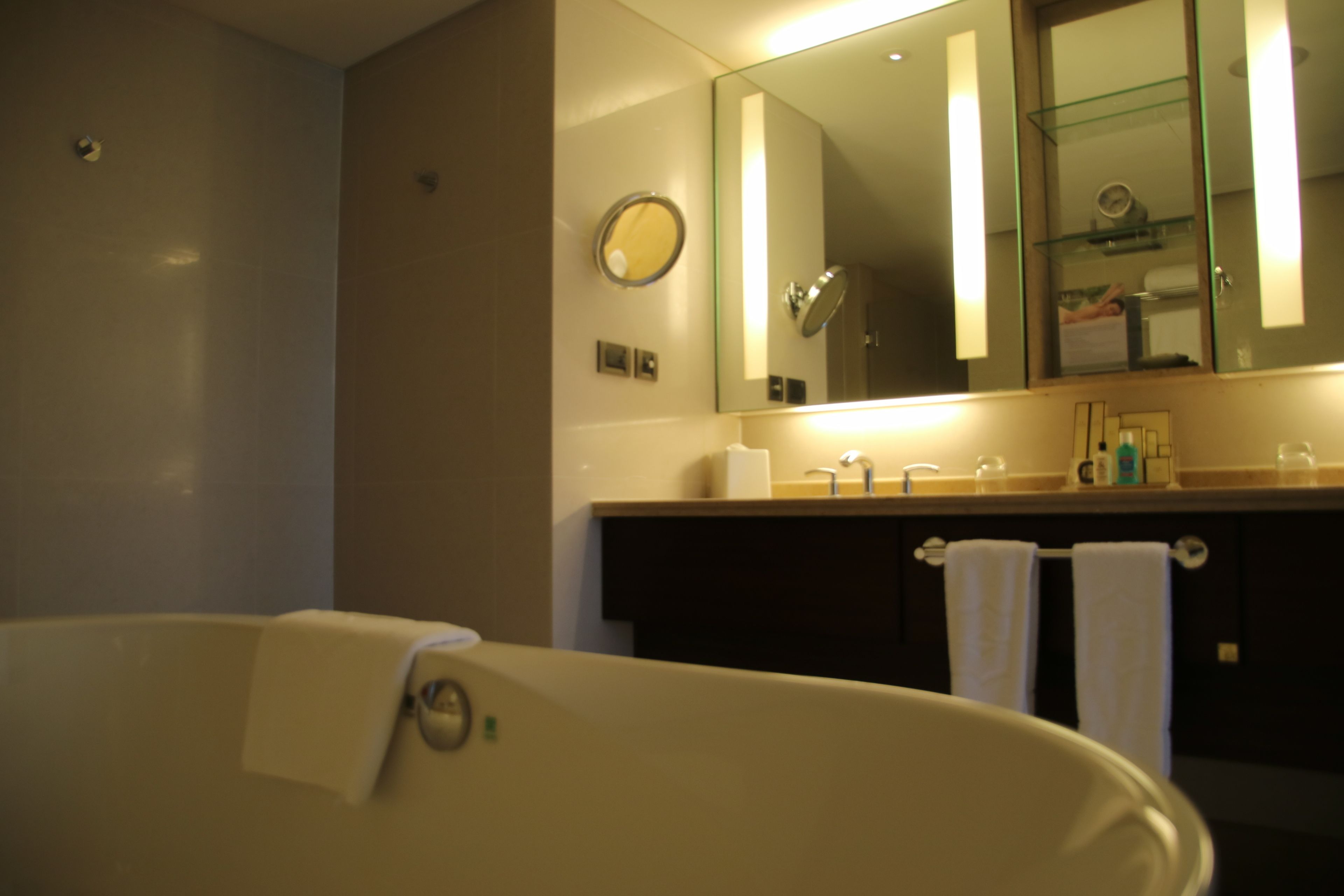 A modern bathroom with a freestanding bathtub, a large mirror, and a vanity with a glass shelf.