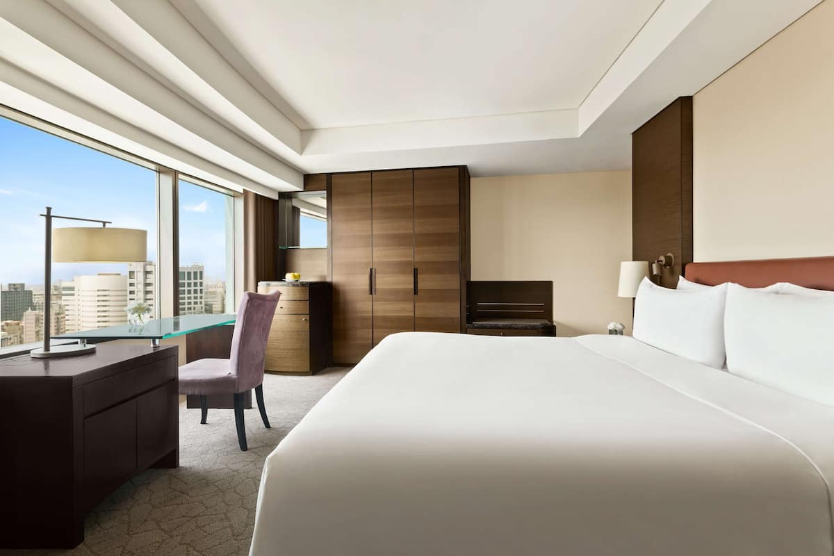 Een hotelkamer met een groot bed, een bureau met stoel, een kledingkast en uitzicht op de stad.