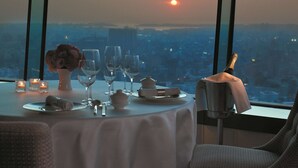Ein Tisch für zwei Personen mit Blick auf einen Sonnenuntergang über einer Stadtlandschaft.
