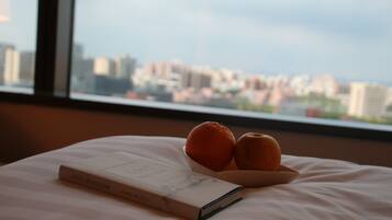 Un libro titulado "Lost Horizon" sobre una cama, con un cuenco que contiene dos naranjas y una manzana.