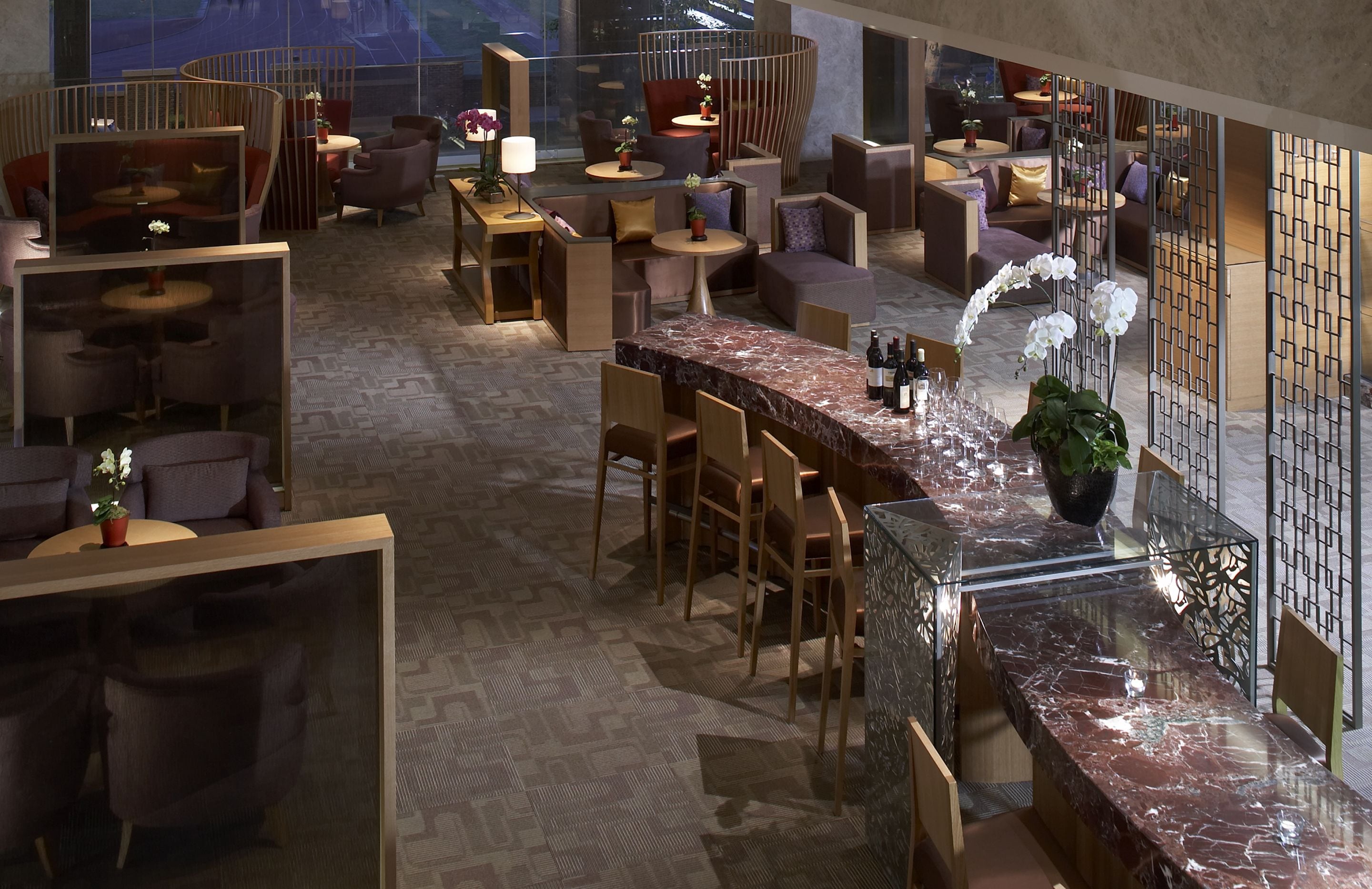 Un área de lounge moderna con disposición de asientos, una barra de mármol y plantas decorativas.