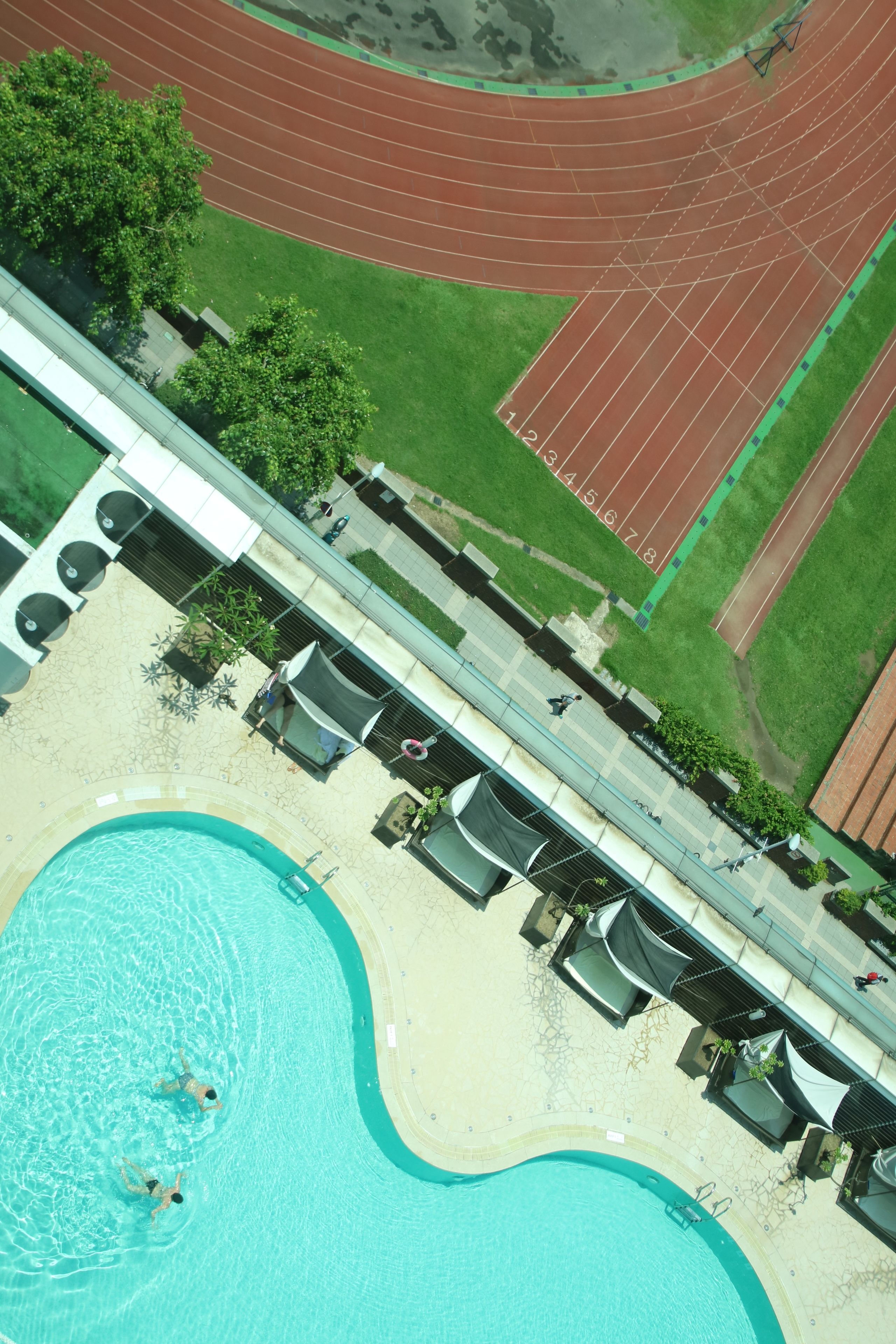 An aerial view of a hotel with a swimming pool, a running track, and outdoor seating.