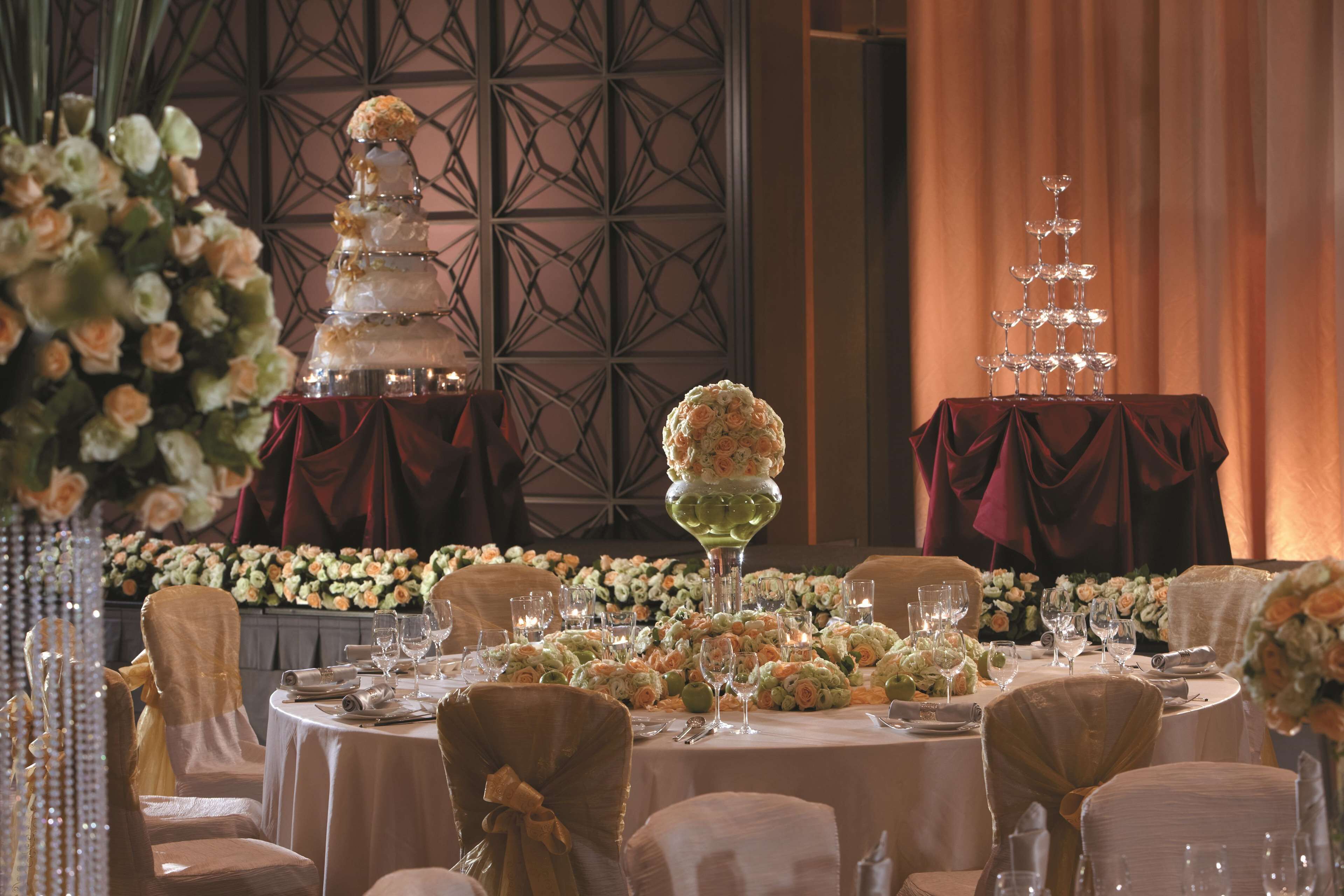 A banquet hall with round tables set for a formal event, featuring tiered floral arrangements and elegant table settings.