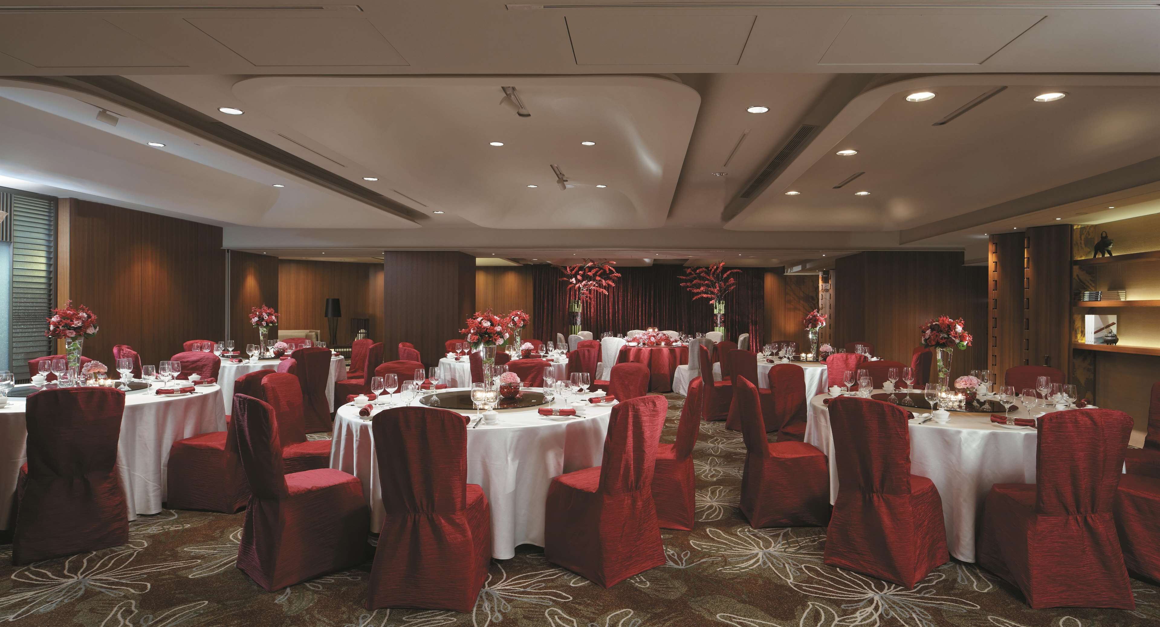 A banquet hall with round tables, red chairs, and floral centerpieces.
