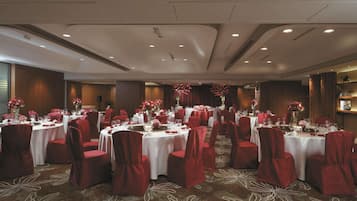 A banquet hall with round tables, red chairs, and floral centerpieces.
