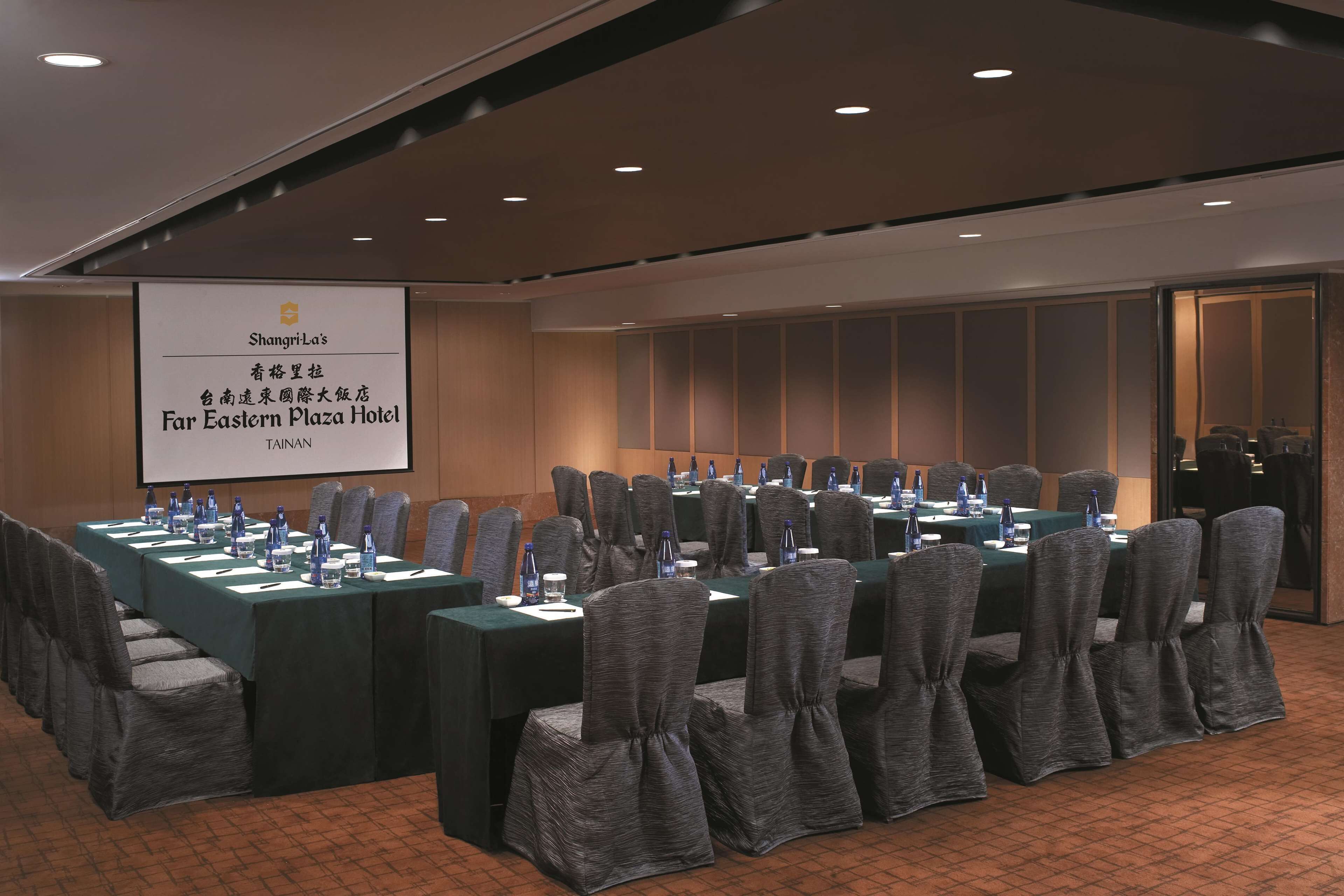 A conference room with a long table, chairs, and a projection screen displaying hotel information.