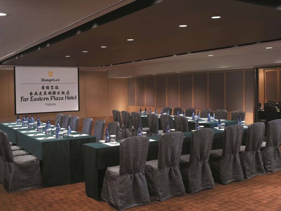 A conference room with a long table, chairs, and a projection screen displaying hotel information.