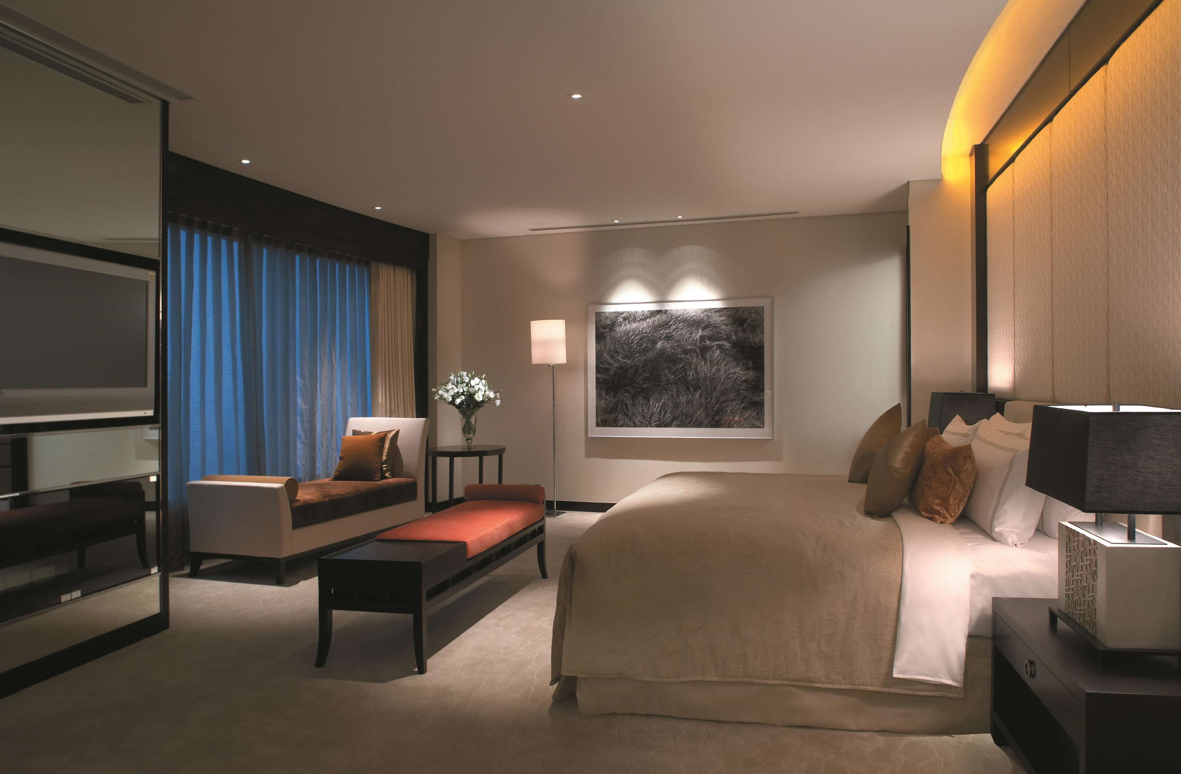 A modern hotel room with a large bed, a sofa, a small table, and a TV.