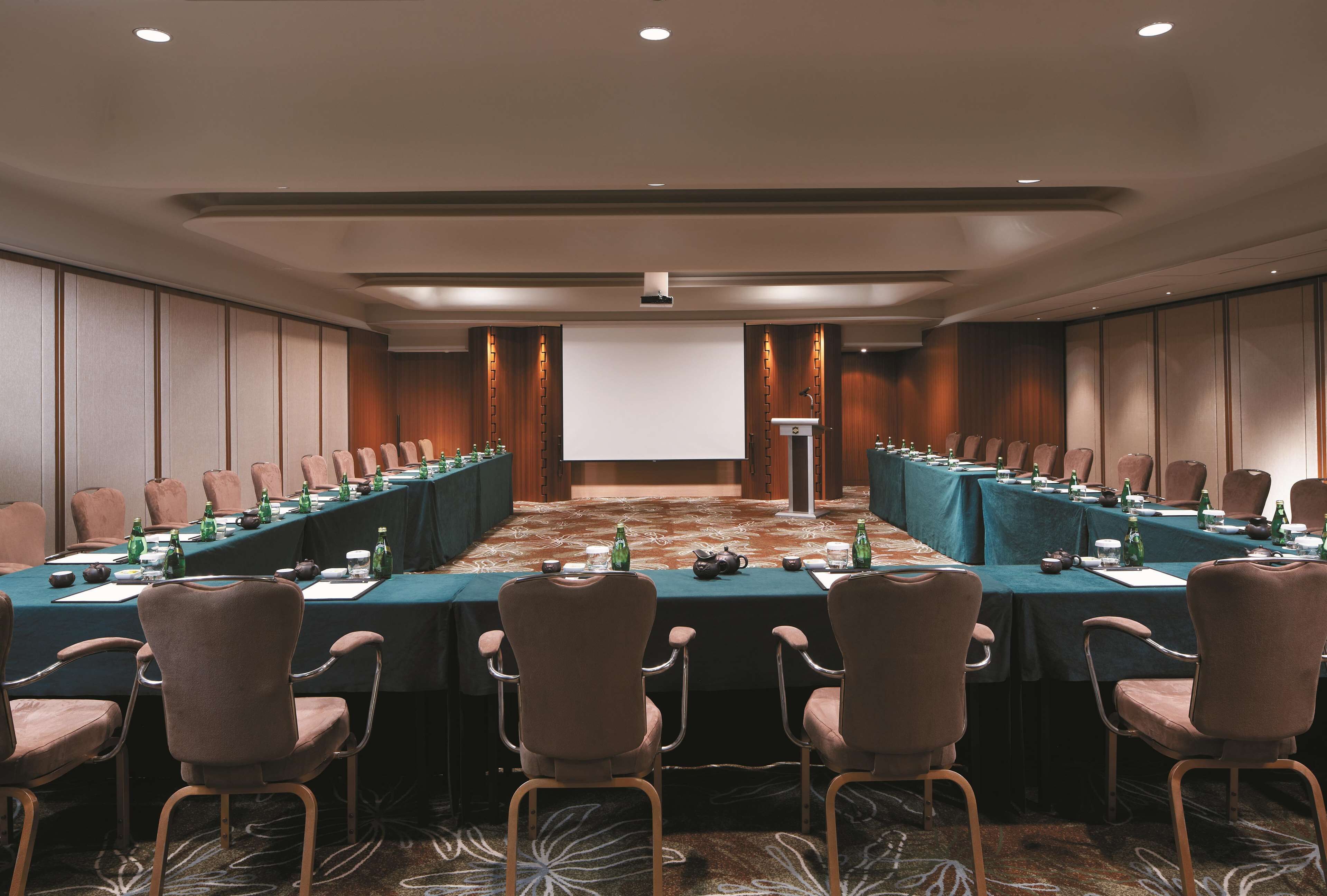 Un salón de conferencias con una mesa larga, sillas y una pantalla para proyector.