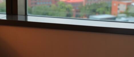 A bed with a book and two fruits, a window with a city view.