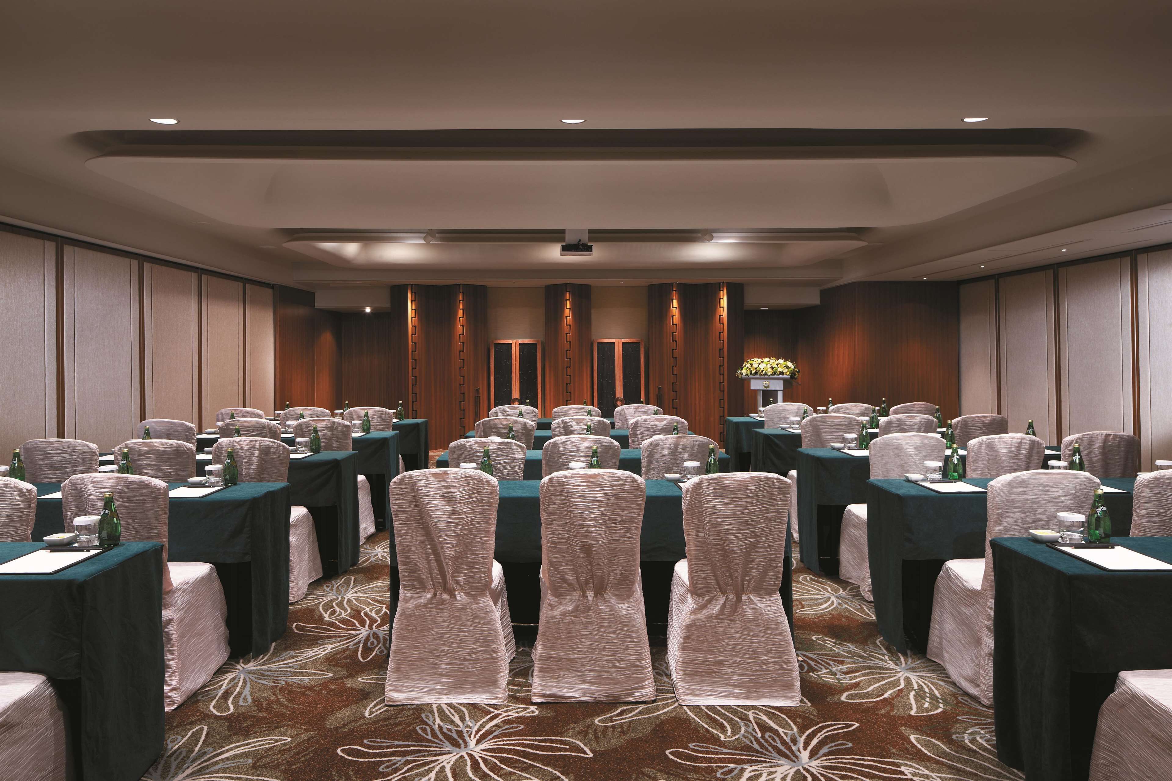 A conference room with rows of tables and chairs, equipped with microphones and water bottles.