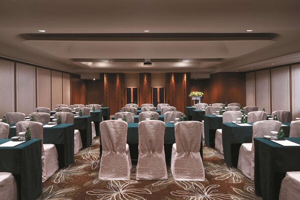 A conference room with rows of tables and chairs, equipped with microphones and water bottles.