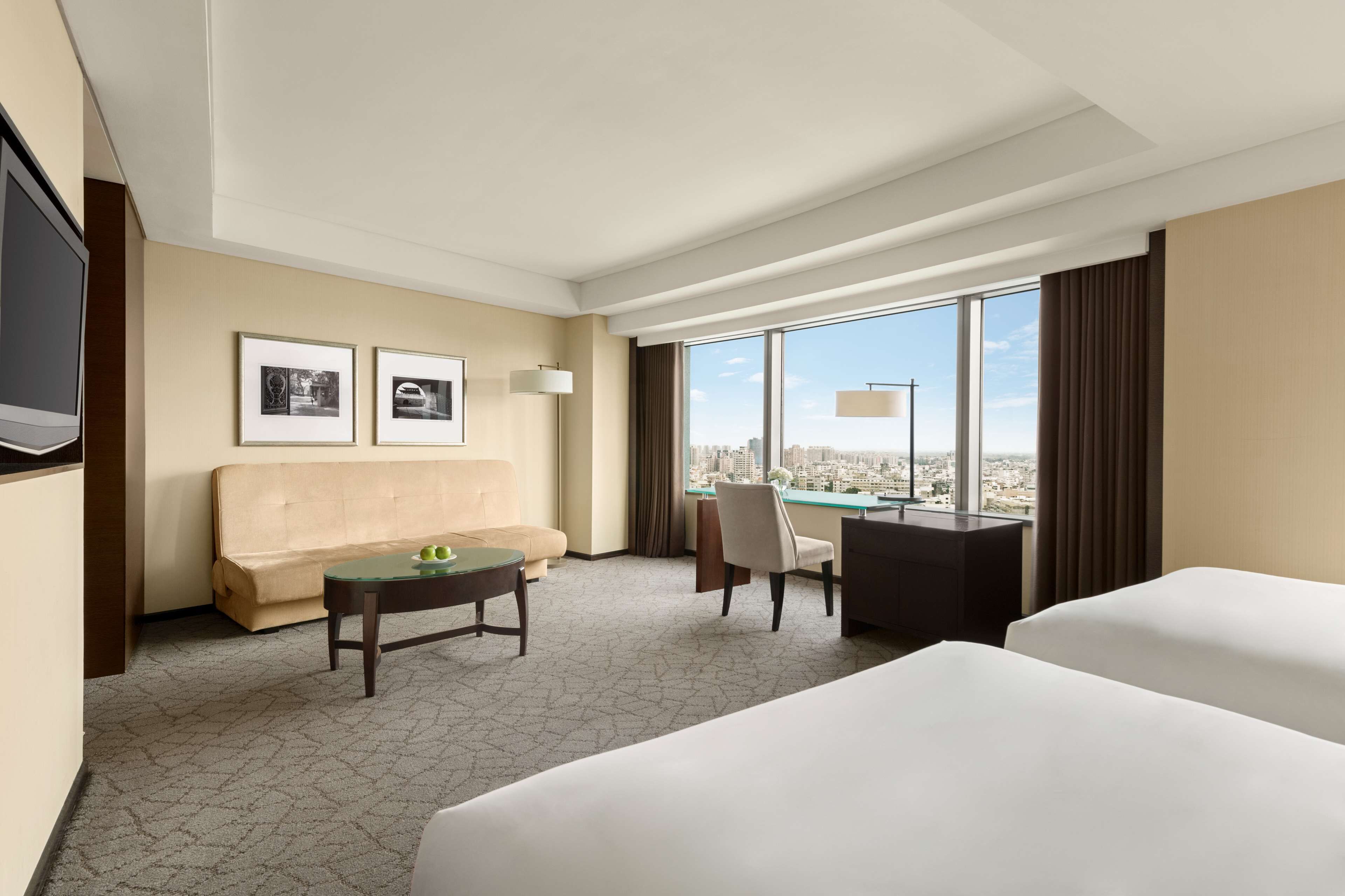 A hotel room with a large bed, a desk, a chair, a sofa, and a TV.