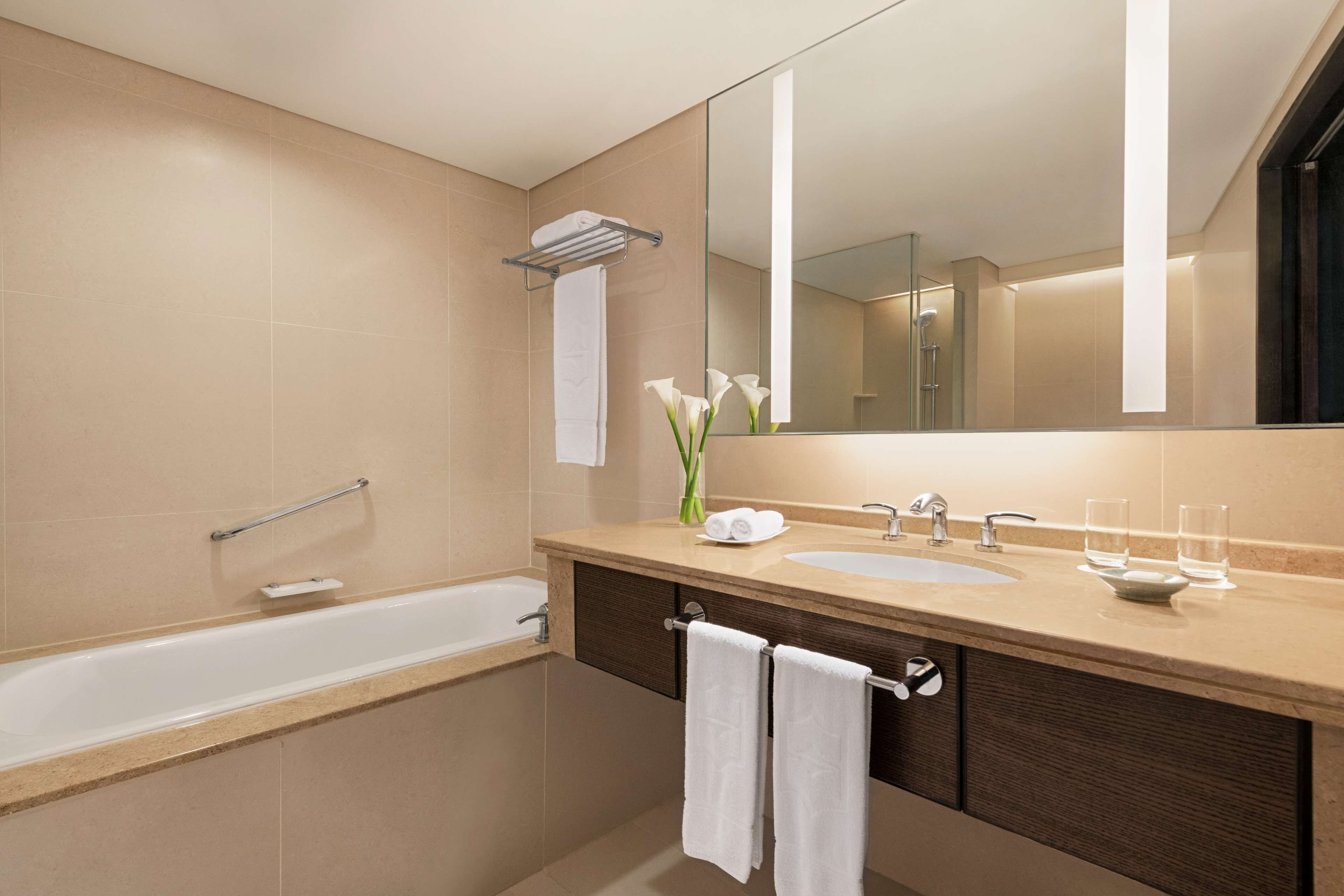A modern bathroom with a bathtub, a sink, a vanity with a mirror, and a towel rack.