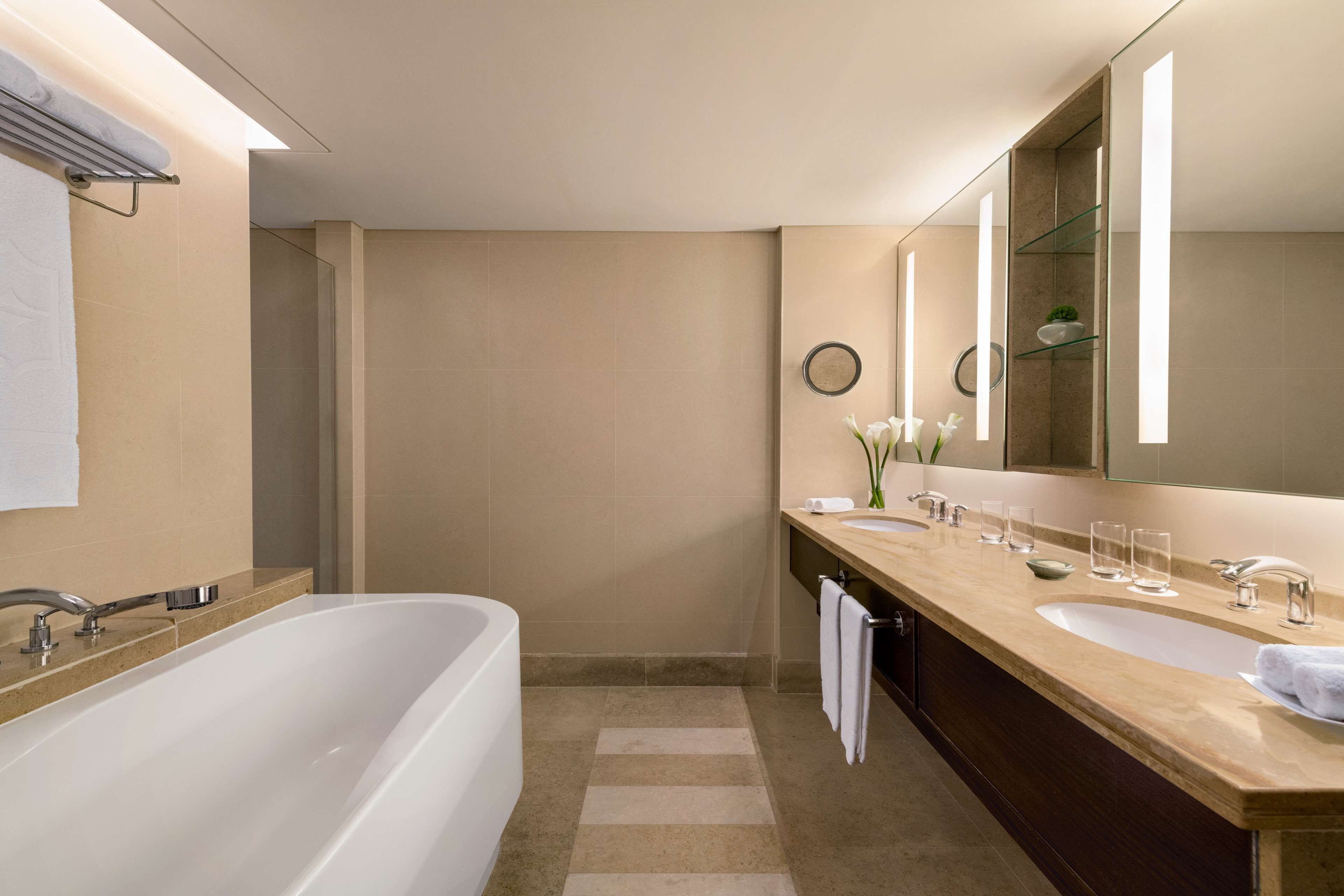 Un baño moderno con una bañera grande, dos lavamanos, un tocador y un espejo amplio.