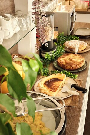A buffet table with various dishes, including a pie, a bowl of soup, and a plate with a piece of meat. - Les Jardins (Lucciana)