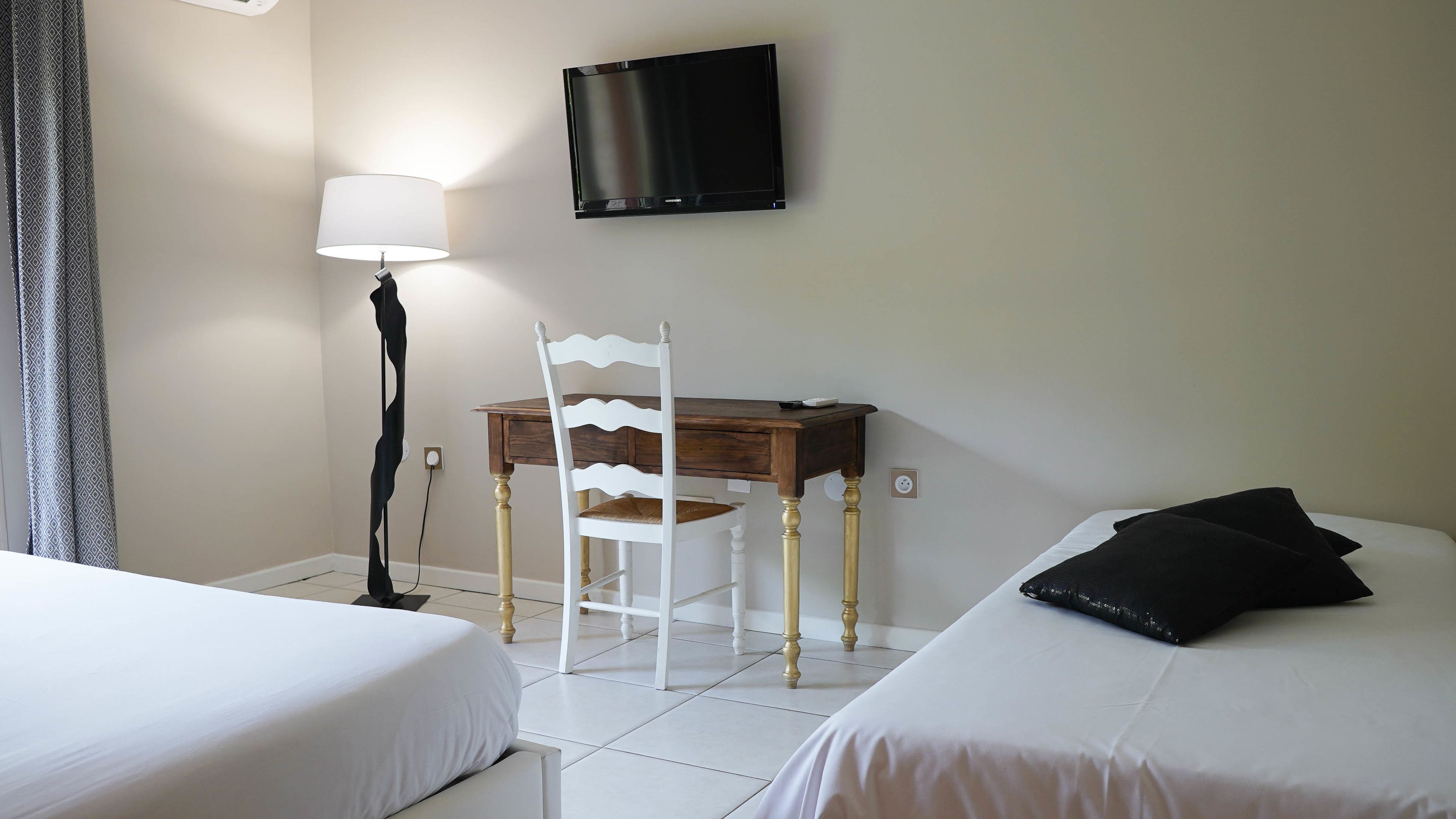 Ein Hotelzimmer mit zwei Betten, einem Schreibtisch, einem Stuhl, einer Lampe und einem Fernseher.