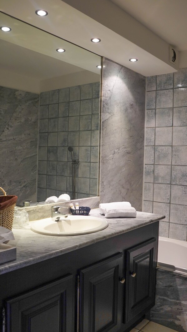 Un baño moderno con lavamanos de mármol, un espejo grande y una zona de ducha.