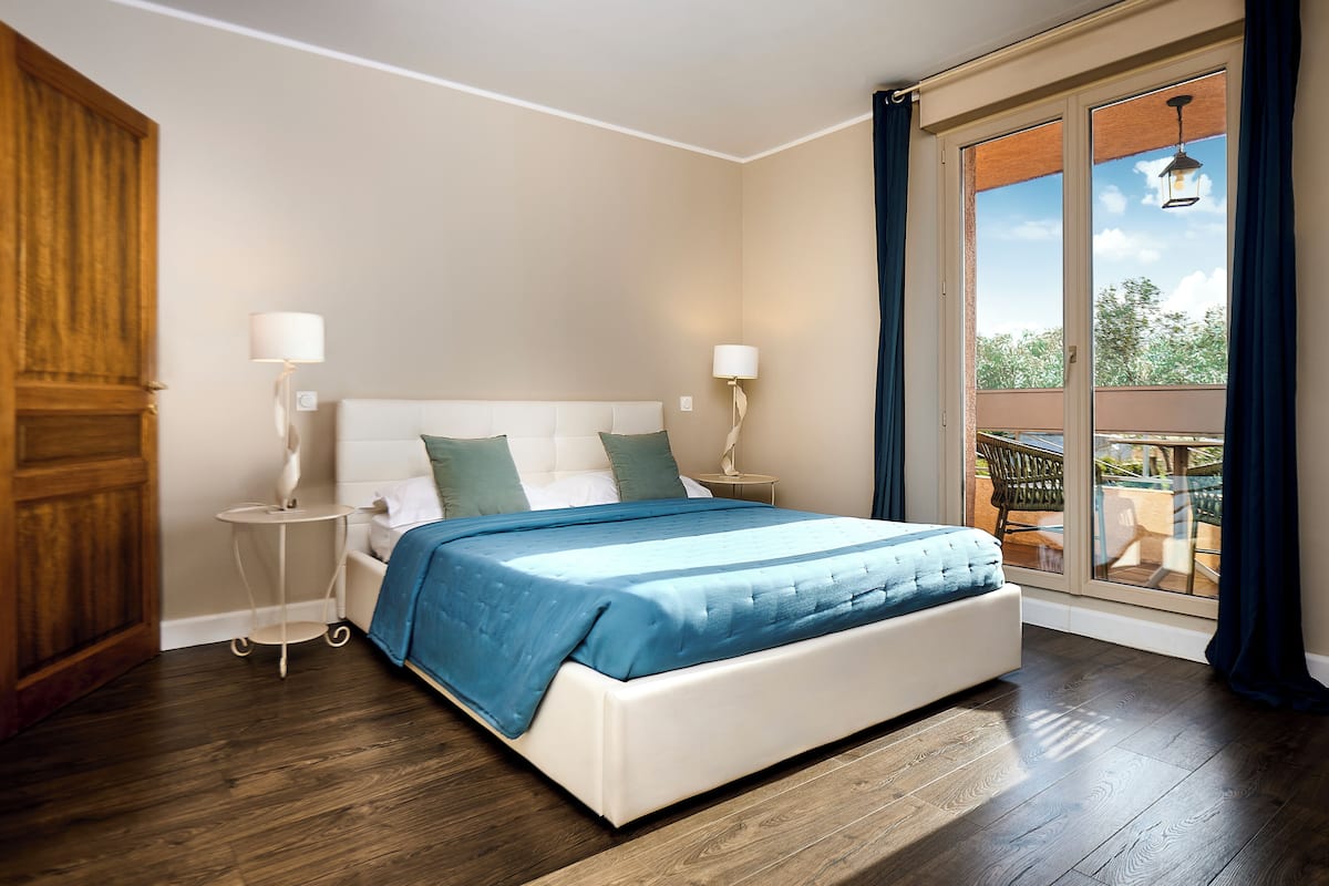 Ein Schlafzimmer mit einem großen Bett, zwei Nachttischen mit Lampen, einem Holzschrank und einem Balkon mit Gartenmöbeln.