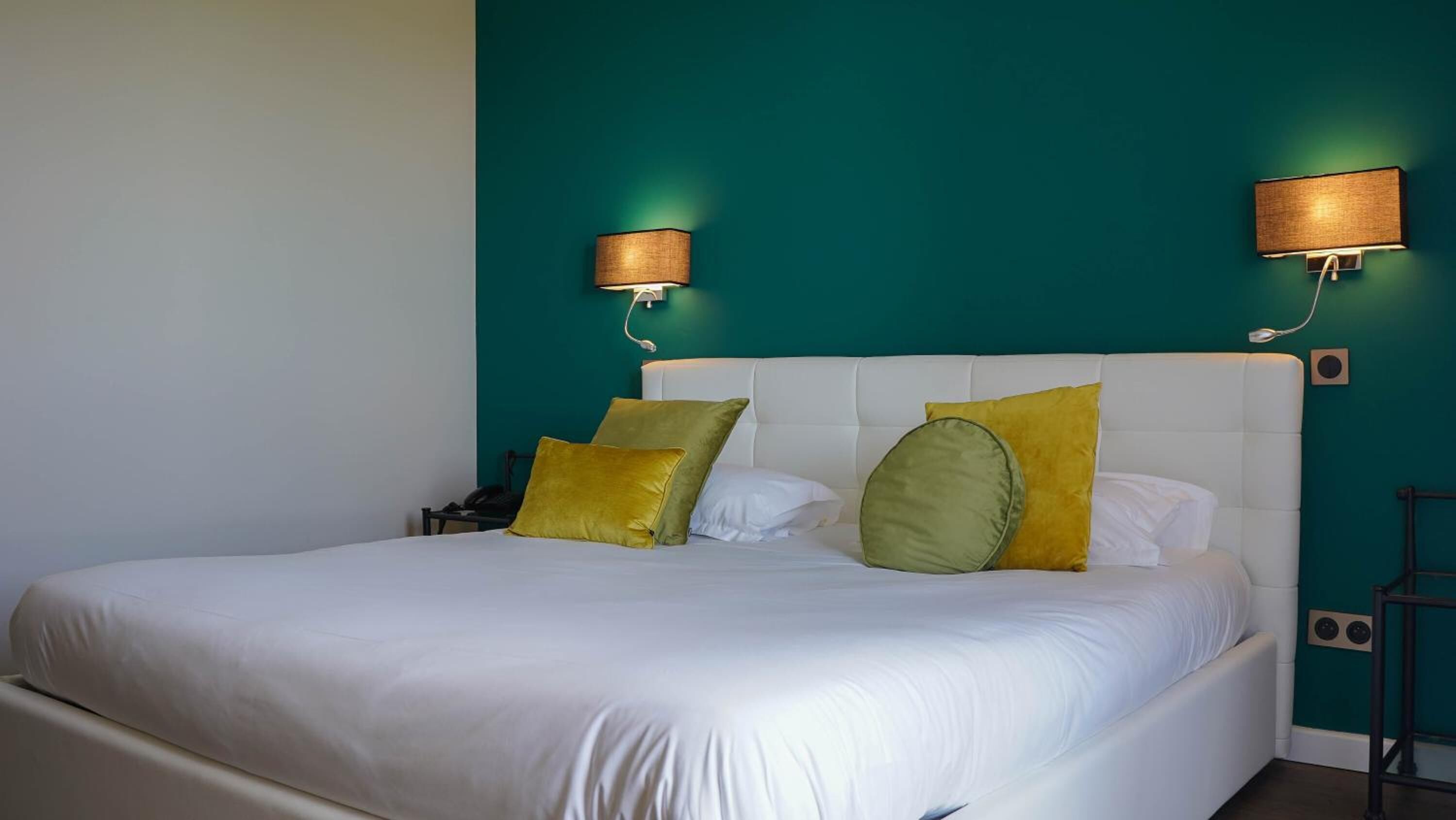 A hotel room with a large bed, teal walls, and two wall-mounted lamps.