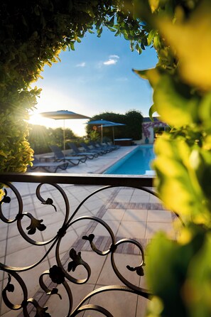 A pool area with lounge chairs and umbrellas, surrounded by greenery. - Les Jardins (Lucciana)