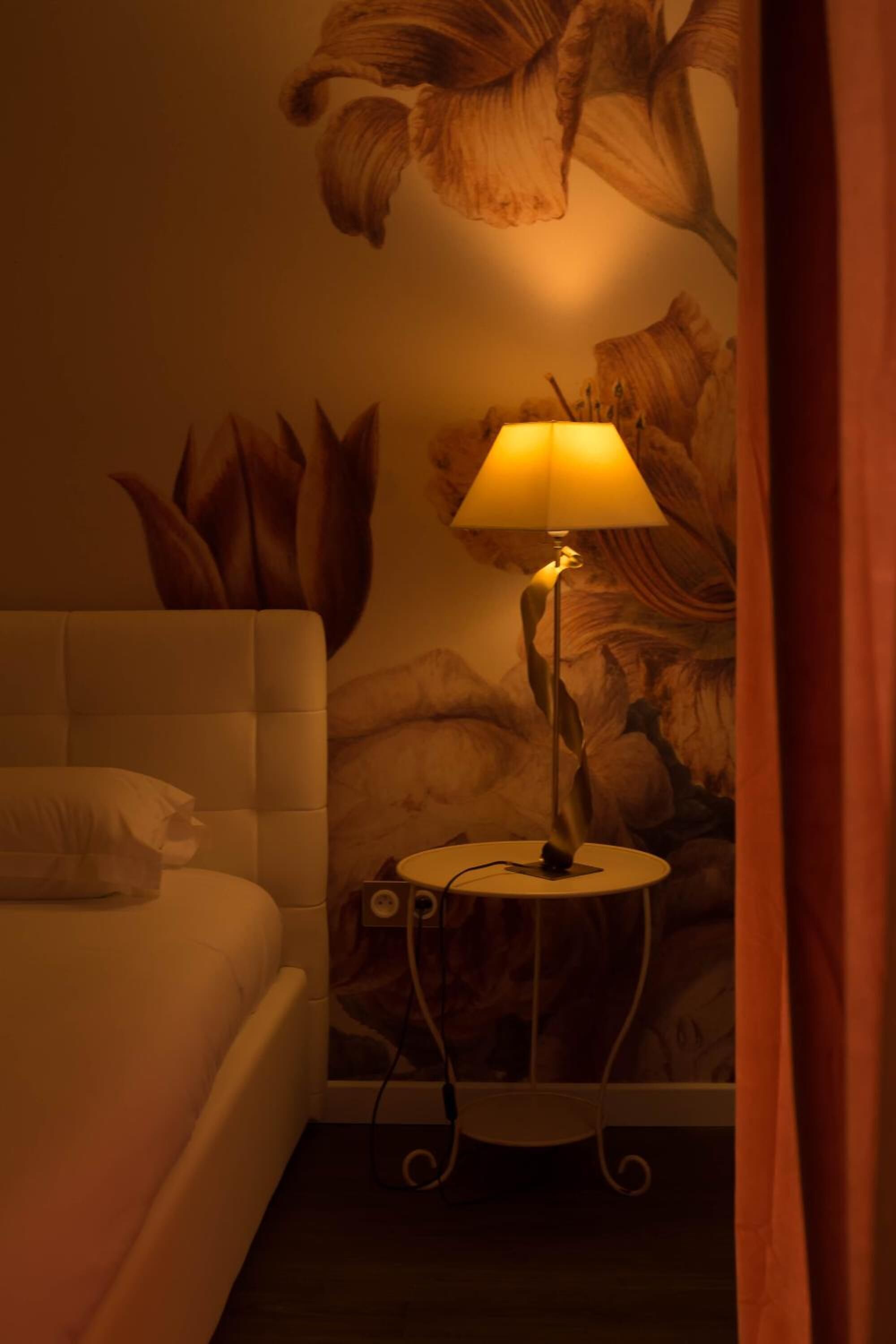 Une chambre d’hôtel avec un lit, une table de chevet avec une lampe et une fresque florale sur le mur.