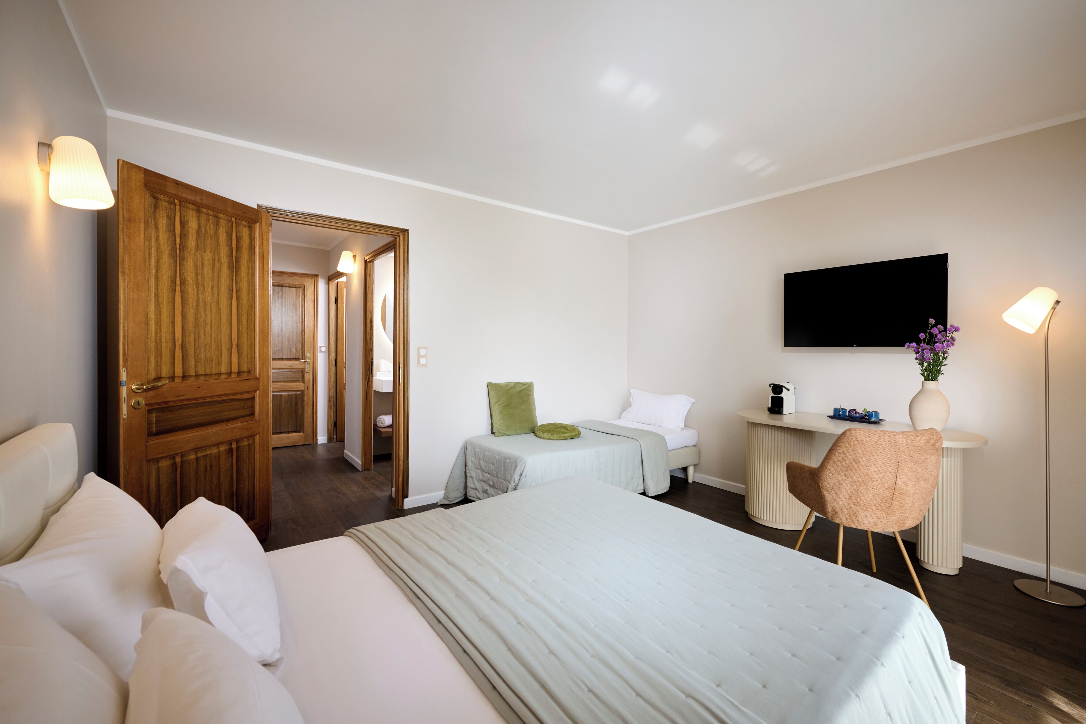 Una camera d'albergo con un letto grande, una scrivania con una sedia, un televisore e una porta che dà su un'altra stanza.