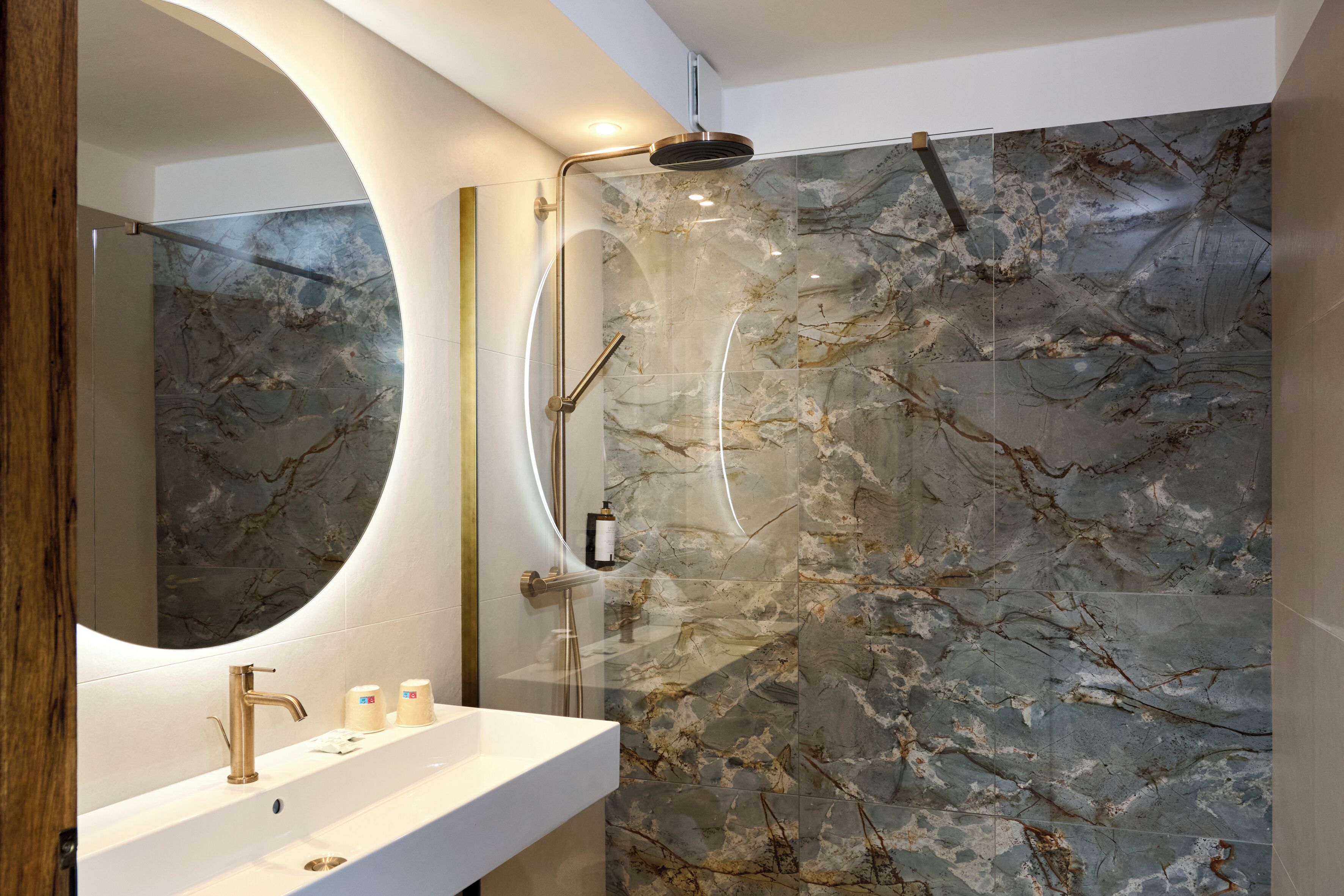 A modern bathroom with a curved mirror, a white sink, and a shower with a glass enclosure.