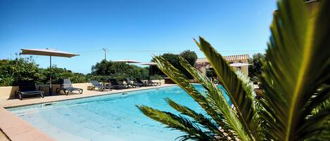 A swimming pool with lounge chairs and umbrellas, surrounded by greenery.