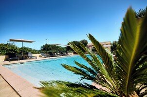 Una piscina con sillones de descanso y sombrillas, rodeada de vegetación.