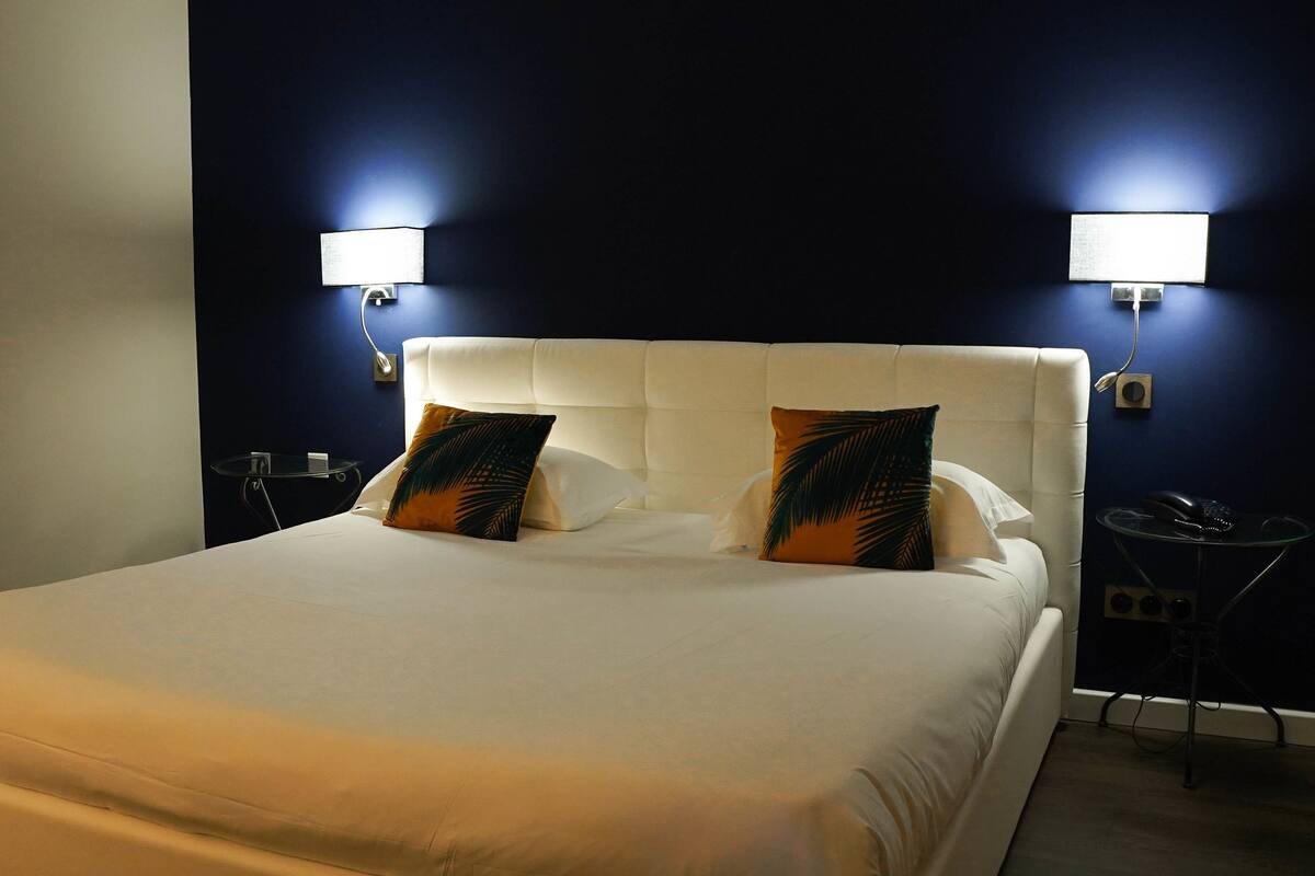 Ein Hotelzimmer mit einem großen Bett, zwei Nachttischlampen, einem kleinen Tisch und einem Telefon.