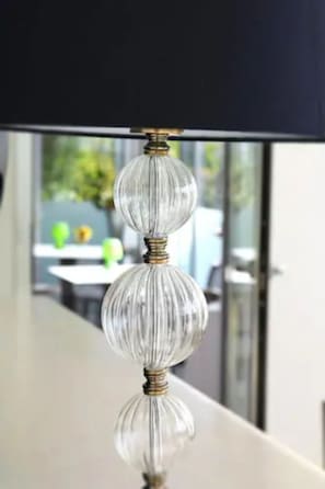 A table lamp sits atop a table, its clear glass shade and metallic base reflecting the surrounding environment.