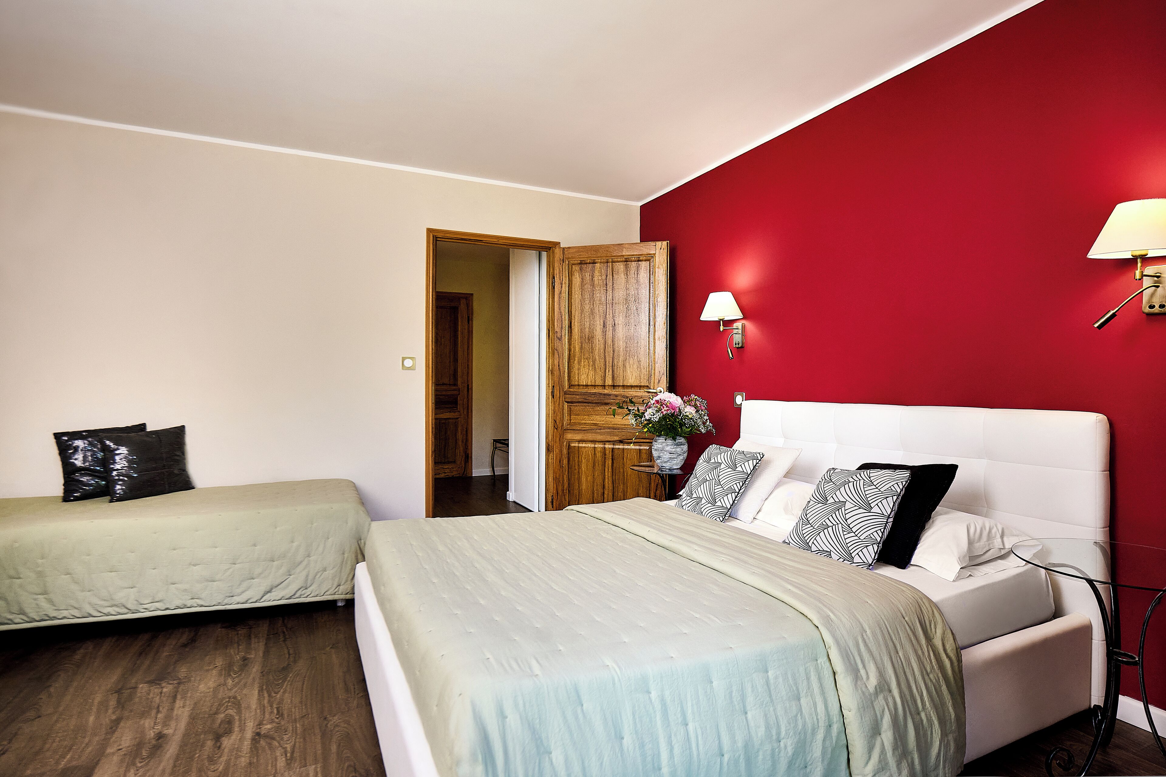 Un dormitorio con dos camas, una pared de acento roja, una puerta de madera y una mesita de noche con lámpara.