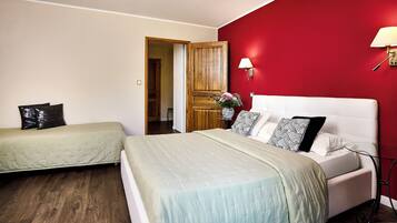 Un dormitorio con dos camas, una pared de acento roja, una puerta de madera y una mesita de noche con lámpara.