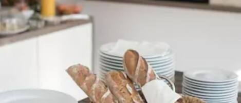 A kitchen counter with stacks of white plates, a wicker basket with bread, and a water dispenser in the background.