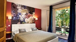 A bedroom with a large bed, two bedside tables, a floral wall mural, and a view of an outdoor garden through a sliding door.