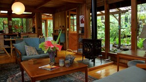 A cozy wooden cabin interior with a sofa, coffee table, and a wood-burning stove. - Volcano Rainforest Retreat (Volcano)