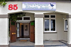 La entrada al Westshore Beach Inn, con un gran letrero con el número 85, una puerta de madera que invita a entrar y un cartel con una ilustración de un pájaro.
