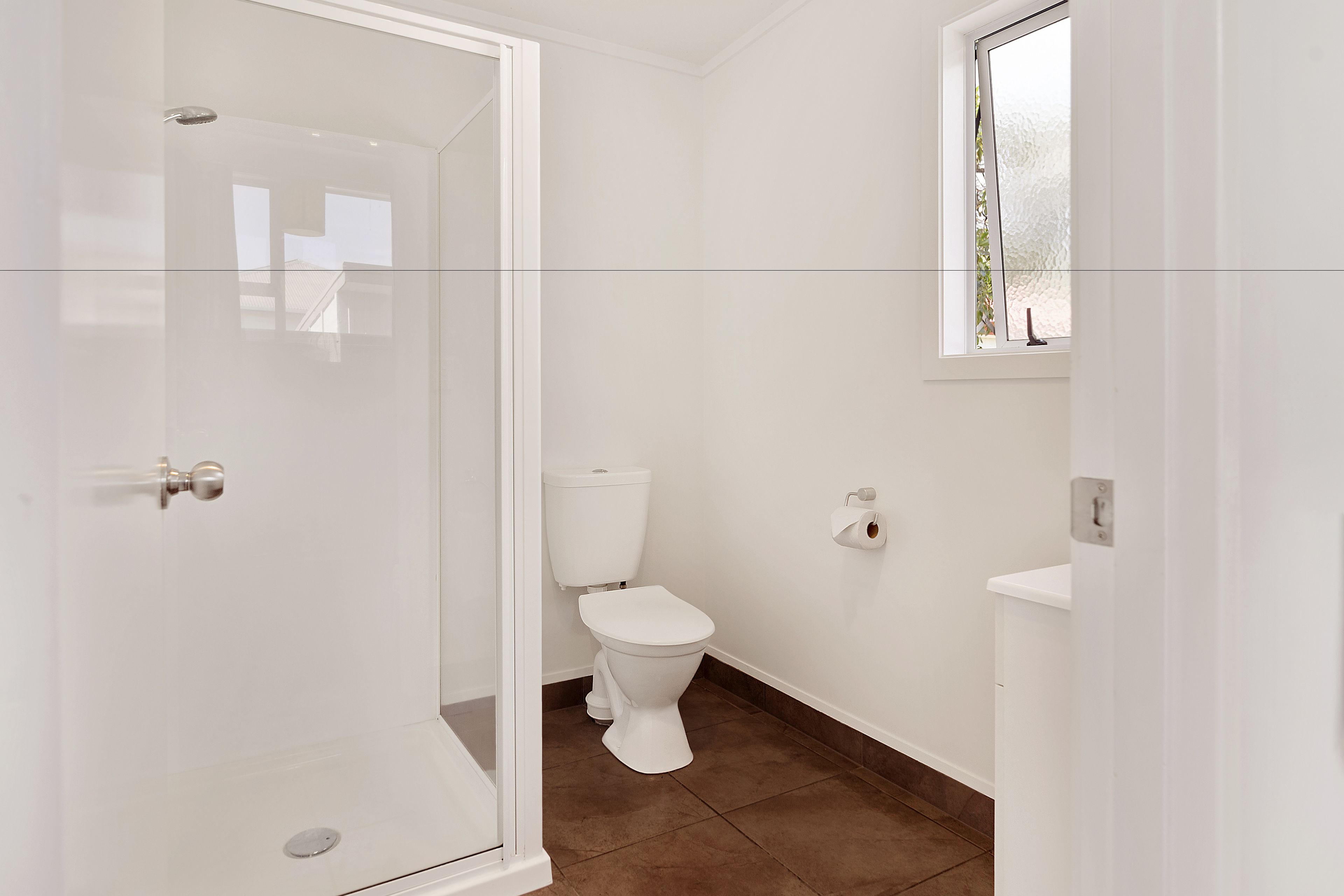 Un baño con cabina de ducha de vidrio, inodoro y ventana.