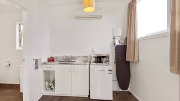 Cocina compacta con armarios blancos, microondas integrado, un refrigerador pequeño y una tetera.