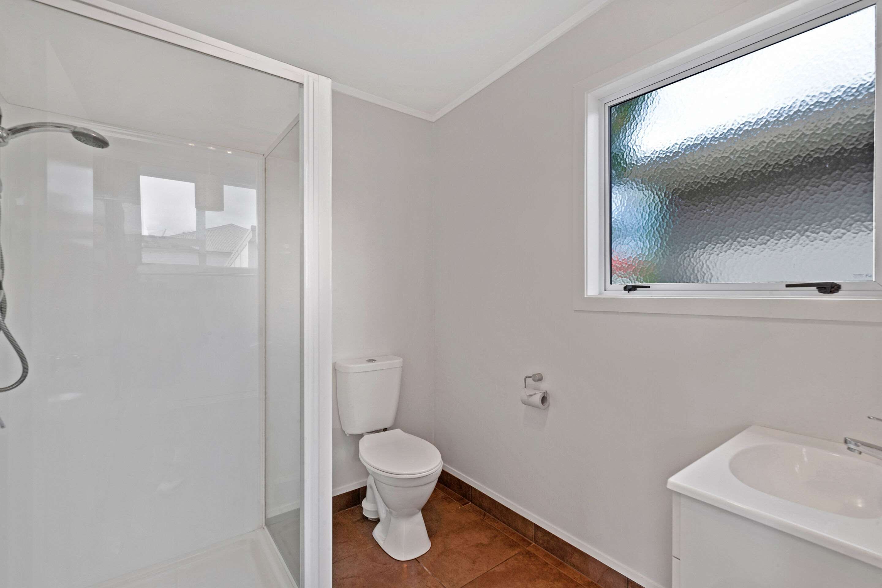 A bathroom with a glass shower enclosure, a toilet, and a sink.
