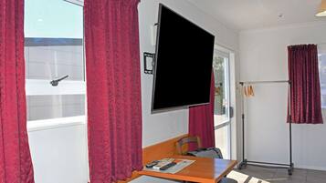 Una habitación con un televisor de pantalla plana grande montado en la pared, una mesa de madera con una silla y una ventana con cortinas rojas.