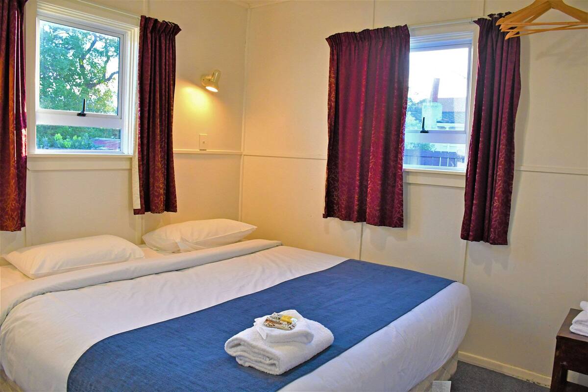 Ein Hotelzimmer mit Bett, einem Fenster mit Vorhängen, einem Nachttisch und einer Wandlampe.