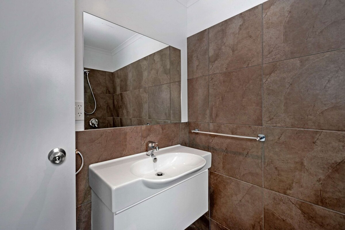 Une salle de bain avec un lavabo blanc, un miroir et des carreaux marron.