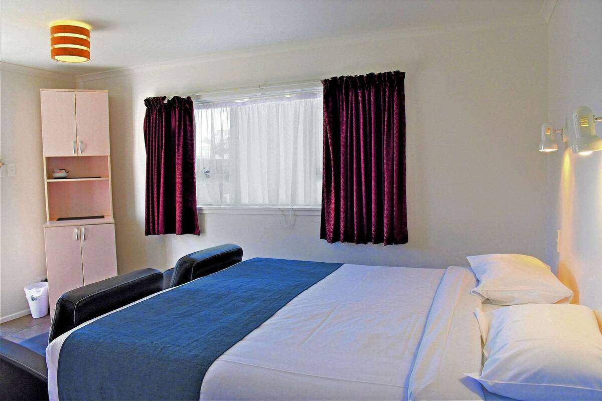 Ein Hotelzimmer mit Bett, Schrank, einem Fenster mit Vorhängen und einer Nachttischlampe.