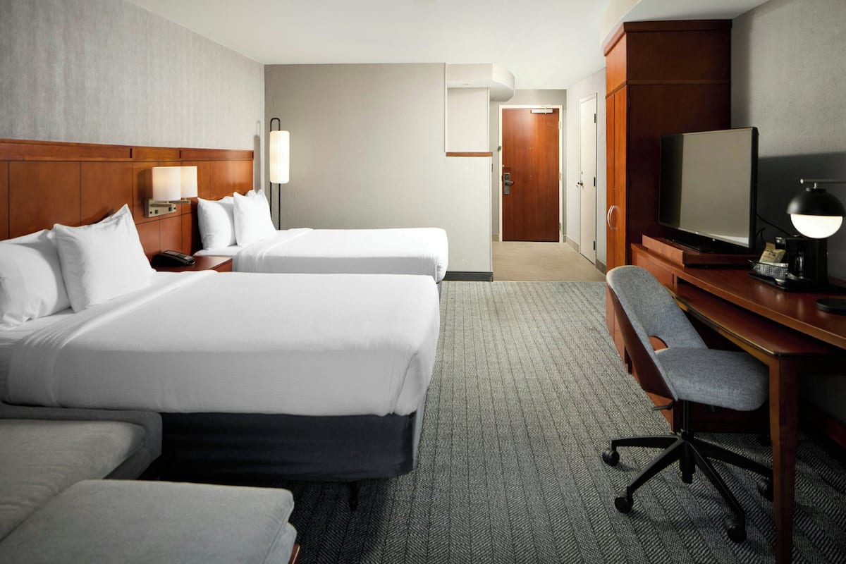 Ein Hotelzimmer mit zwei Betten, einem Schreibtisch, einem Fernseher und einem Sessel.