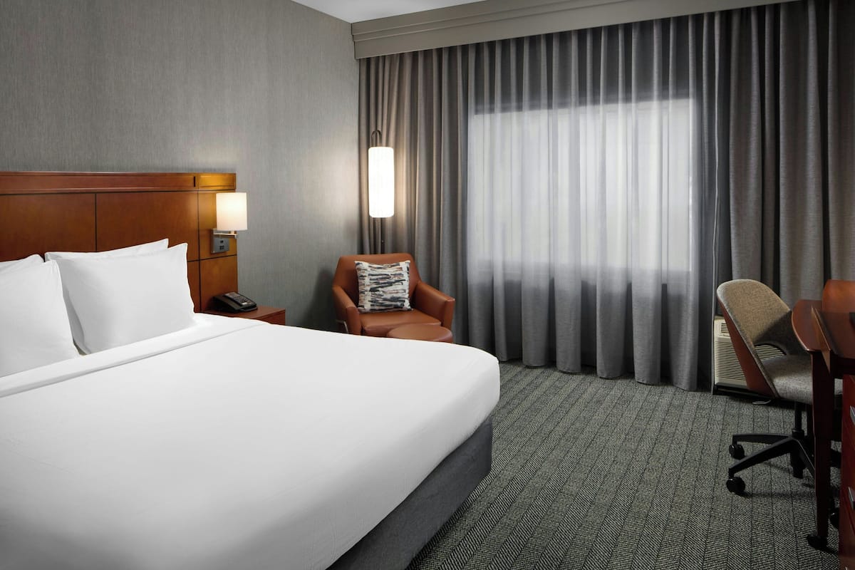 Ein Hotelzimmer mit einem großen Bett, einem Nachttisch mit Lampe, einem Sessel und einem Schreibtisch.